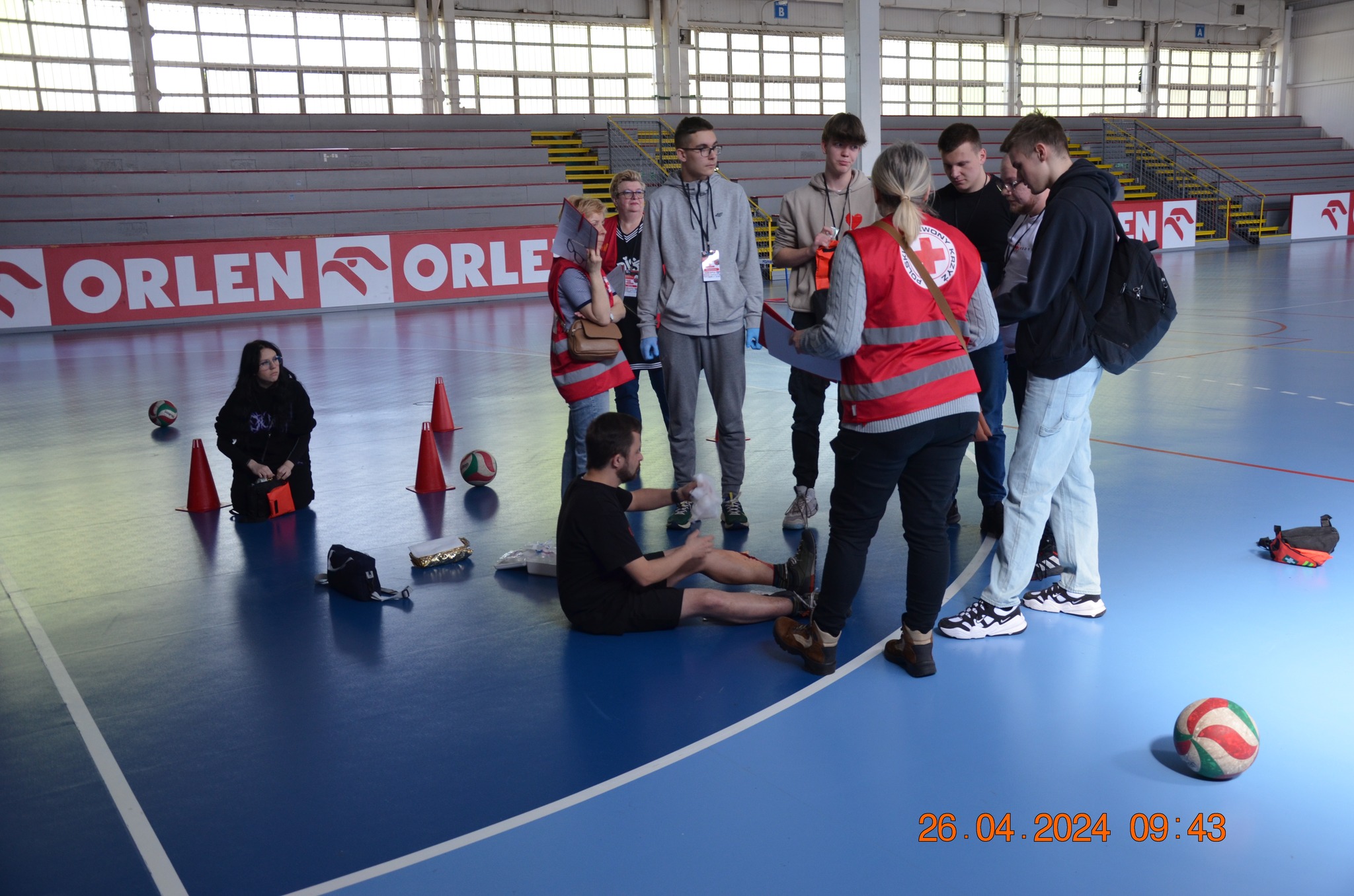 Uczestnicy etapu rejonowego XXX Ogólnopolskich Mistrzostw Pierwszej Pomocy PCK w Płocku udzielają pomocy pozorowanemu poszkodowanemu na hali sportowej.