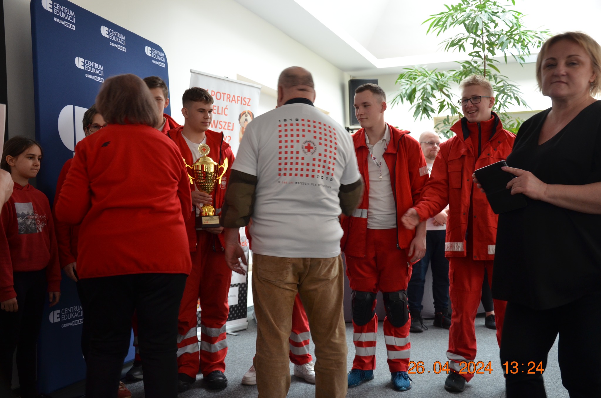 Uczestnicy etapu rejonowego XXX Ogólnopolskich Mistrzostw Pierwszej Pomocy PCK w Płocku w czerwonych strojach ratowniczych odbierają puchar podczas ceremonii zakończenia zawodów.