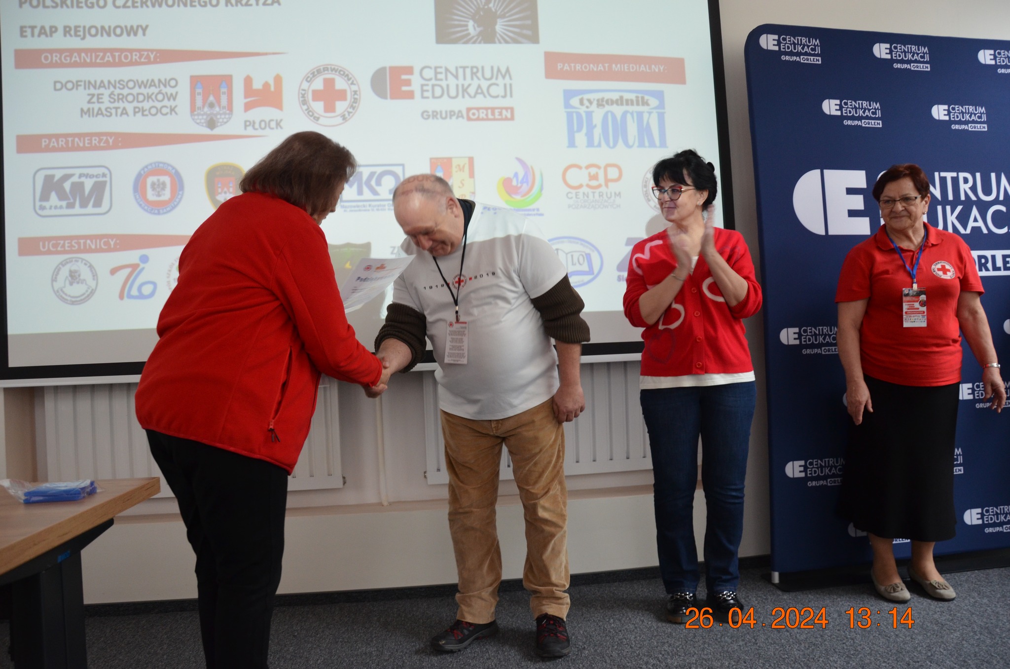 Osoba w koszulce Polskiego Czerwonego Krzyża odbiera dyplom podczas ceremonii zakończenia etapu rejonowego XXX Ogólnopolskich Mistrzostw Pierwszej Pomocy PCK w Płocku.