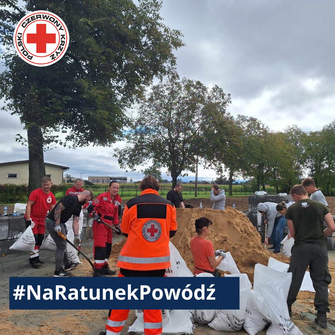 Wolontariusze Polskiego Czerwonego Krzyża i mieszkańcy napełniają worki z piaskiem, przygotowując zabezpieczenia przeciwpowodziowe w ramach akcji #NaRatunekPowódź.