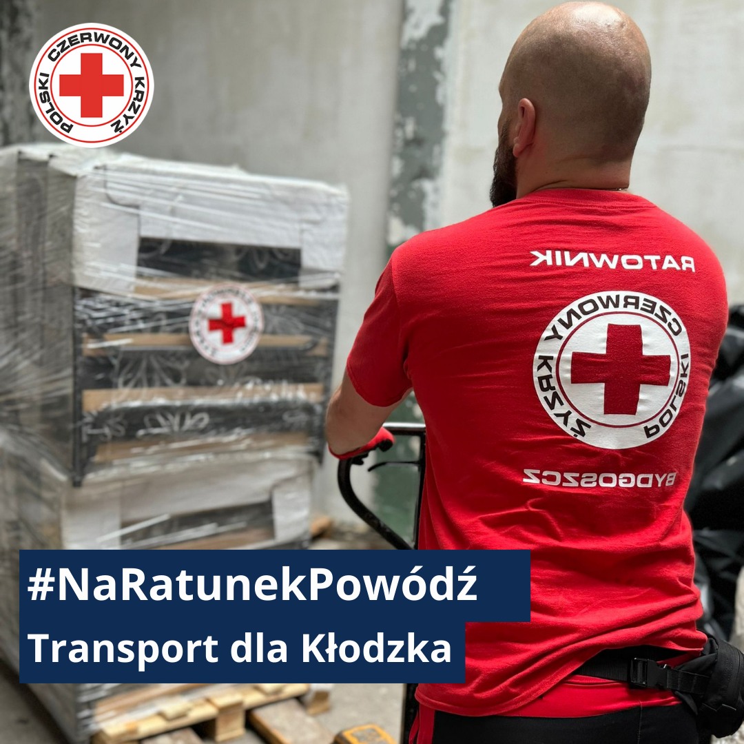 Ratownik Polskiego Czerwonego Krzyża transportuje paletę z pomocą humanitarną oznaczoną logo PCK dla poszkodowanych w powodzi w Kłodzku.