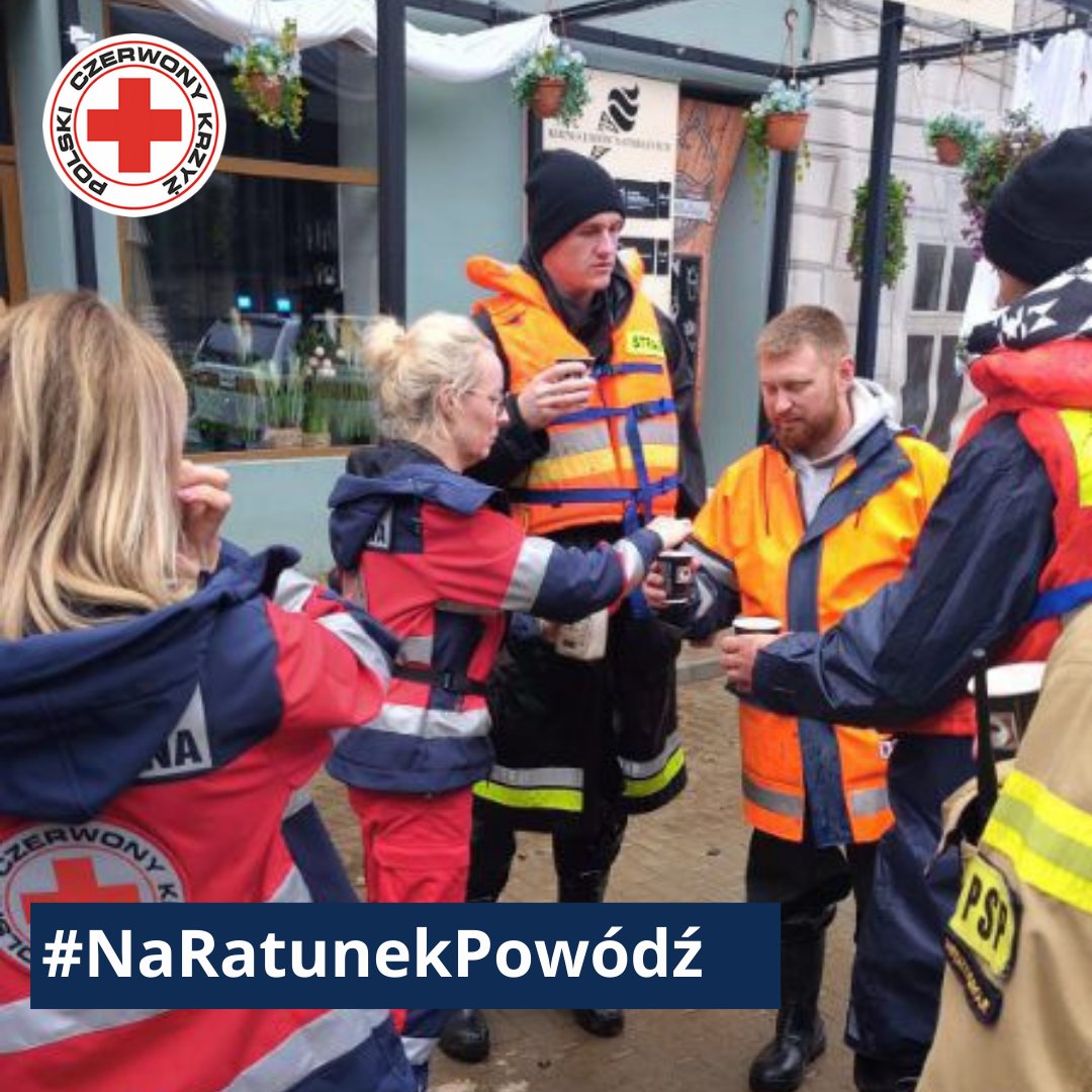 Ratownicy Polskiego Czerwonego Krzyża i służb mundurowych udzielają wsparcia i rozdają ciepłe napoje podczas akcji pomocowej po powodzi.
