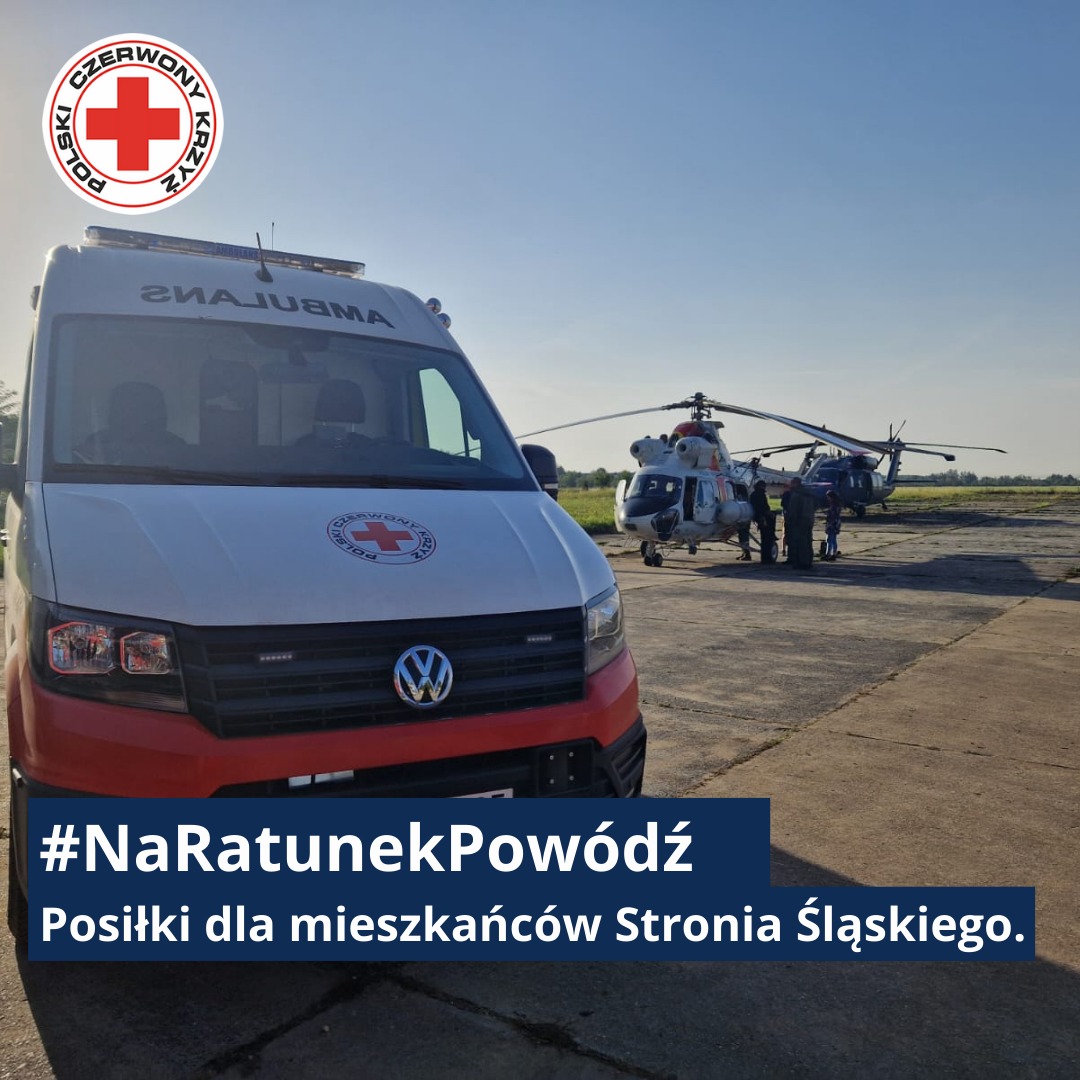 Karetka Polskiego Czerwonego Krzyża oraz śmigłowiec ratunkowy stoją na płycie lotniska podczas akcji dostarczania pomocy poszkodowanym mieszkańcom Stronia Śląskiego po powodzi.