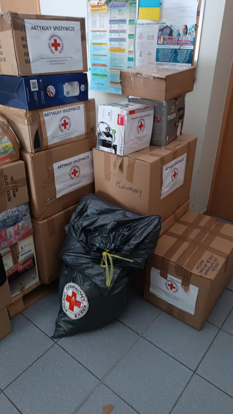Stos kartonów i worków z darami oznaczonych logo Polskiego Czerwonego Krzyża, przygotowanych jako pomoc rzeczowa dla poszkodowanych.