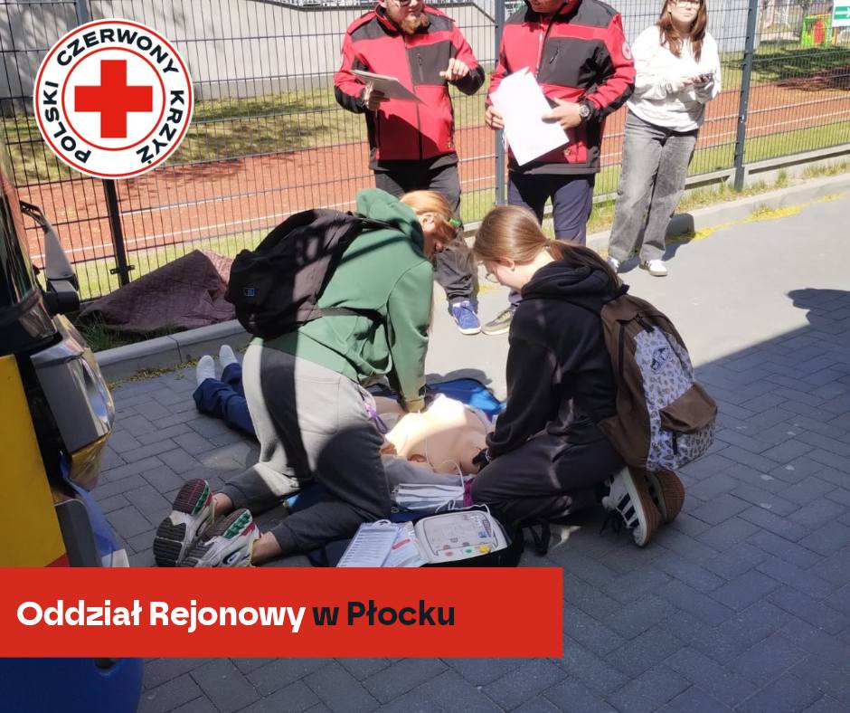 Uczestnicy XXXII Mistrzostw Pierwszej Pomocy PCK w Płocku ćwiczą resuscytację na fantomie pod okiem instruktorów na zewnątrz budynku.