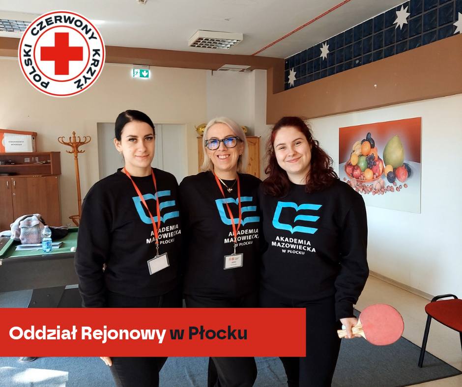 Trzy wolontariuszki w bluzach „Akademia Mazowiecka w Płocku” pozują do zdjęcia podczas XXXII Mistrzostw Pierwszej Pomocy PCK – etap rejonowy w Płocku 2026.