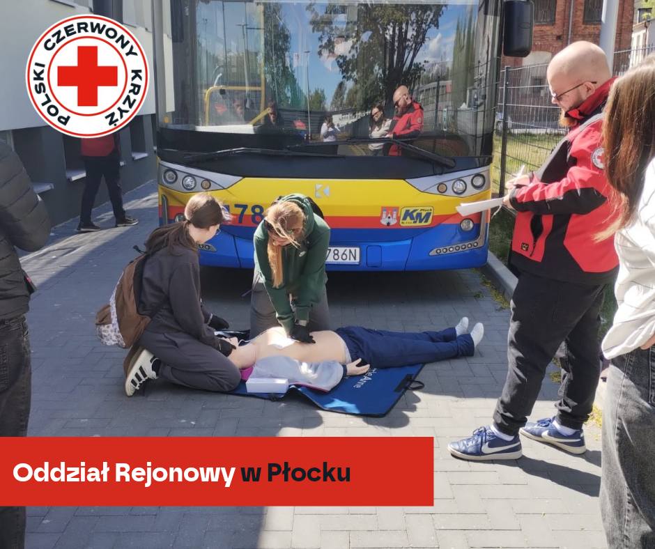 Uczestnicy XXXII Mistrzostw Pierwszej Pomocy PCK w Płocku ćwiczą resuscytację krążeniowo‑oddechową na fantomie przed autobusem miejskim.