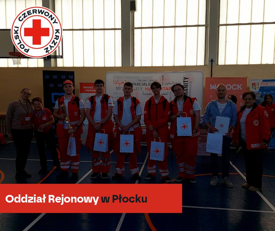 Grupa młodych ratowników i opiekunów PCK w czerwonych strojach pozuje z pucharami i torbami z logo Polskiego Czerwonego Krzyża podczas XXXII Mistrzostw Pierwszej Pomocy – etap rejonowy w Płocku.